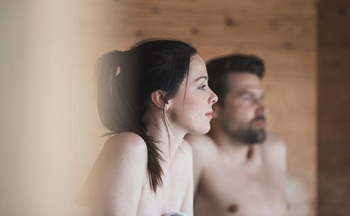 Man and woman relaxing in a wooden sauna, evoking wellness and indoor climate control themes.
