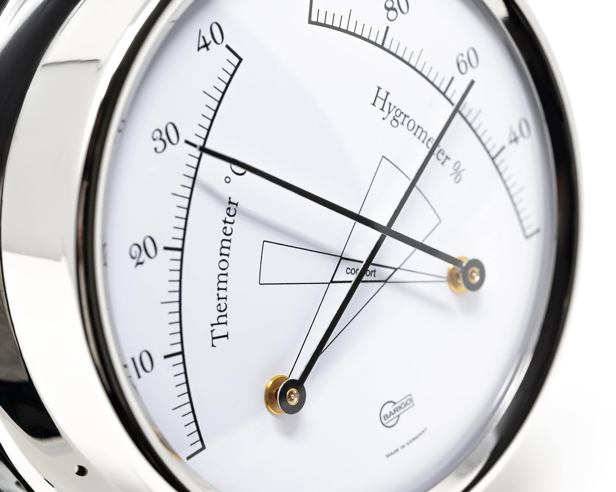 Close-up of a German-made analog thermometer and hygrometer dial with chrome trim.