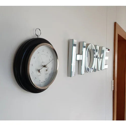 Wall-mounted round barometer with metal frame next to silver HOME letters in hallway