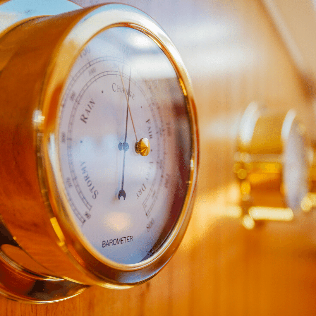 Gold analog barometer mounted on wood panel, classic weather instrument display