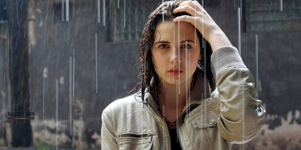 Woman standing in heavy rain with wet hair, wearing a light-colored jacket, outdoors