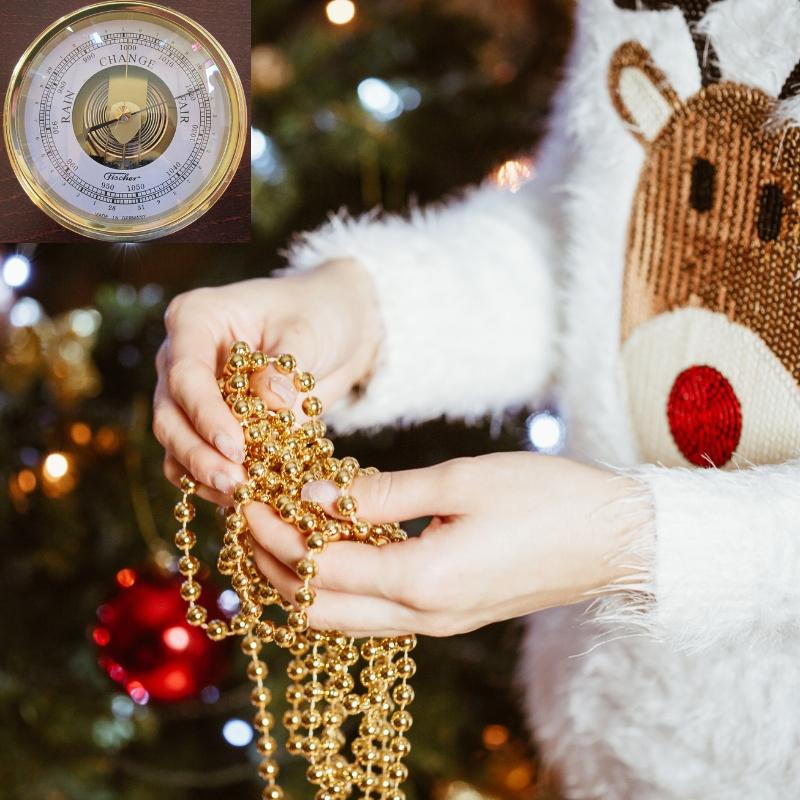 Analog barometer with gold trim, festive setting, person holding gold beads near Christmas tree