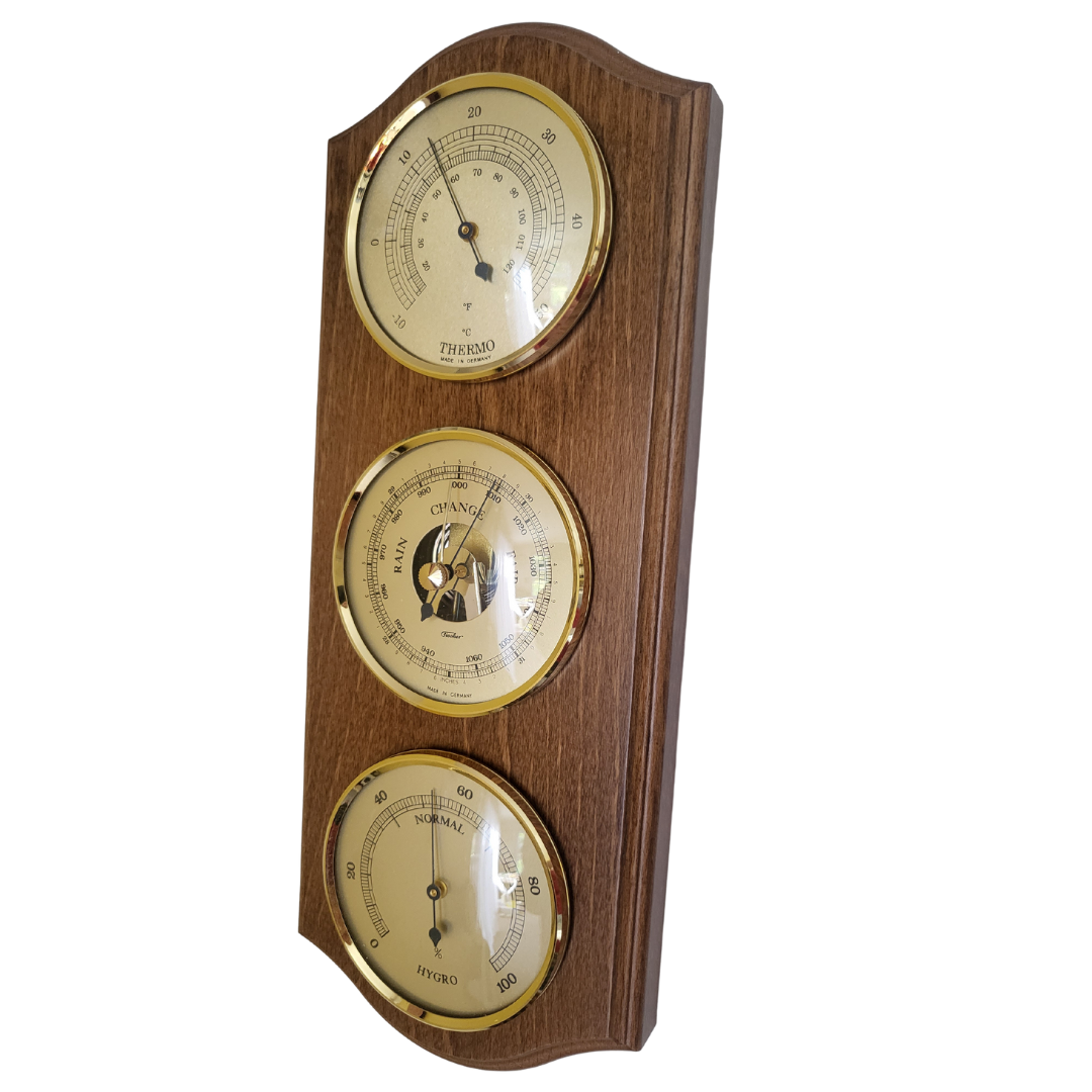 A rustic oak and brass weatherstation with hygrometer, barometer, and thermometer, wall-mounted, vertically oriented.